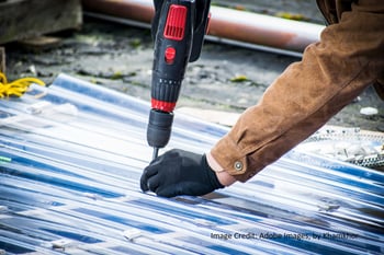 a metal roofer replaces screws on a corrugated metal roof