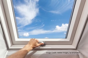 a skylight showing a blue sky in the background; man's hand holding the latch