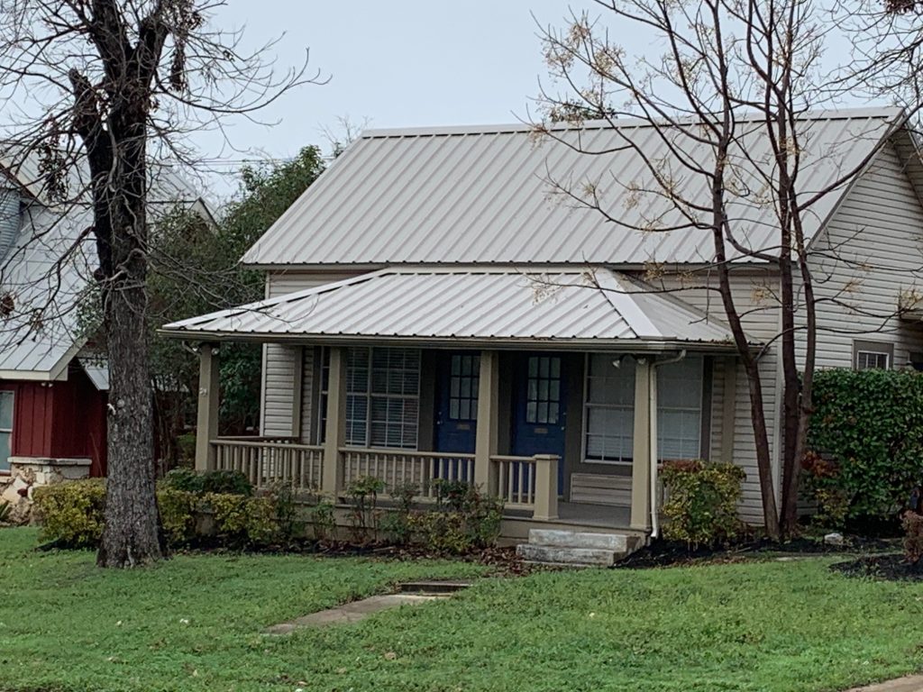 Charming bungalow with a beige standing seam metal roof installed by Longhorn Roofing, including a matching porch roof.