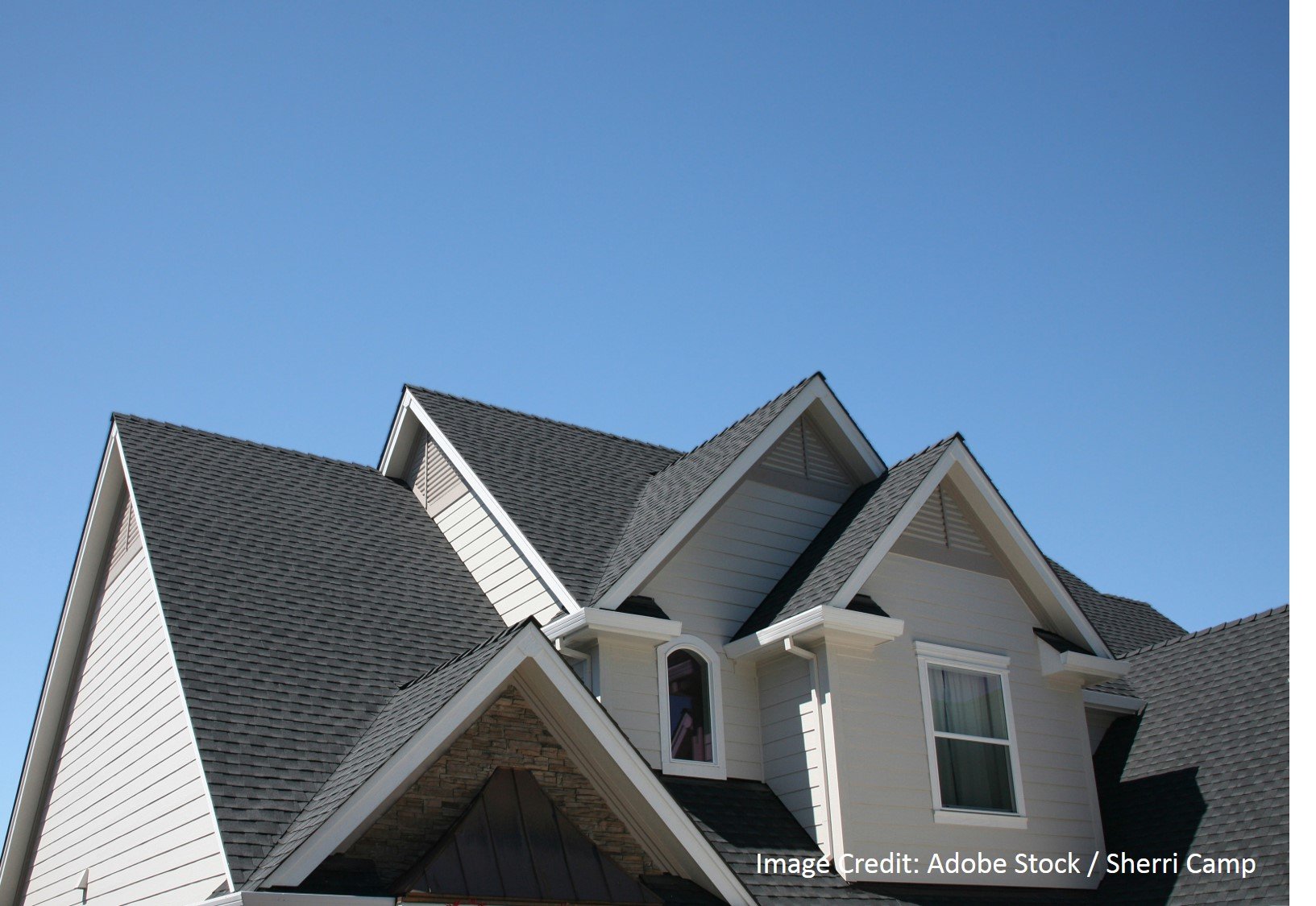 Dark gray dimensional shingle roof with multiple gables, dormers, and white trim set against a clear blue sky.