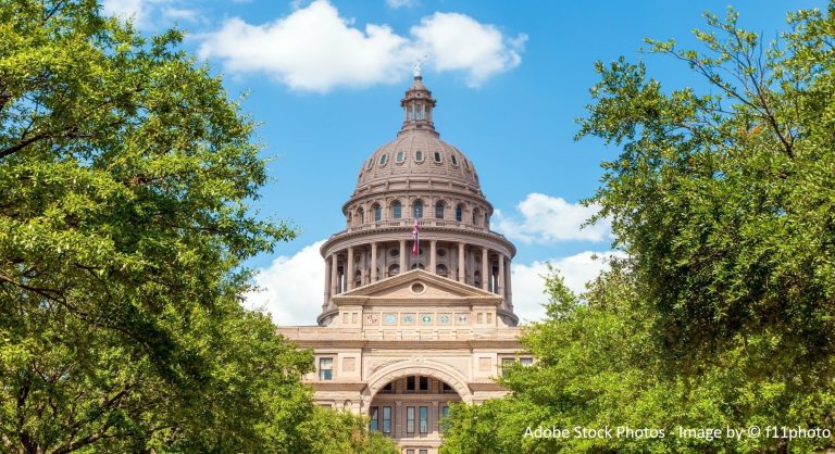 A domed government building rises between two green trees beneath a bright blue sky with scattered clouds.