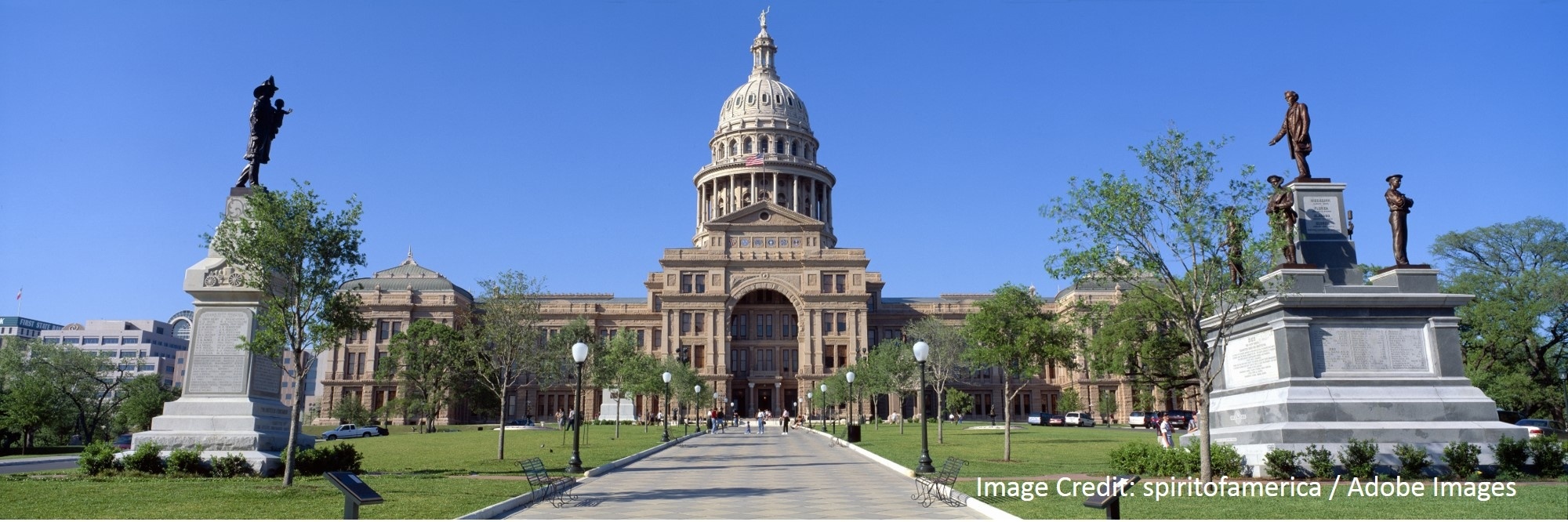 A domed government building rises above a tree-lined walkway flanked by statues and lamp posts.