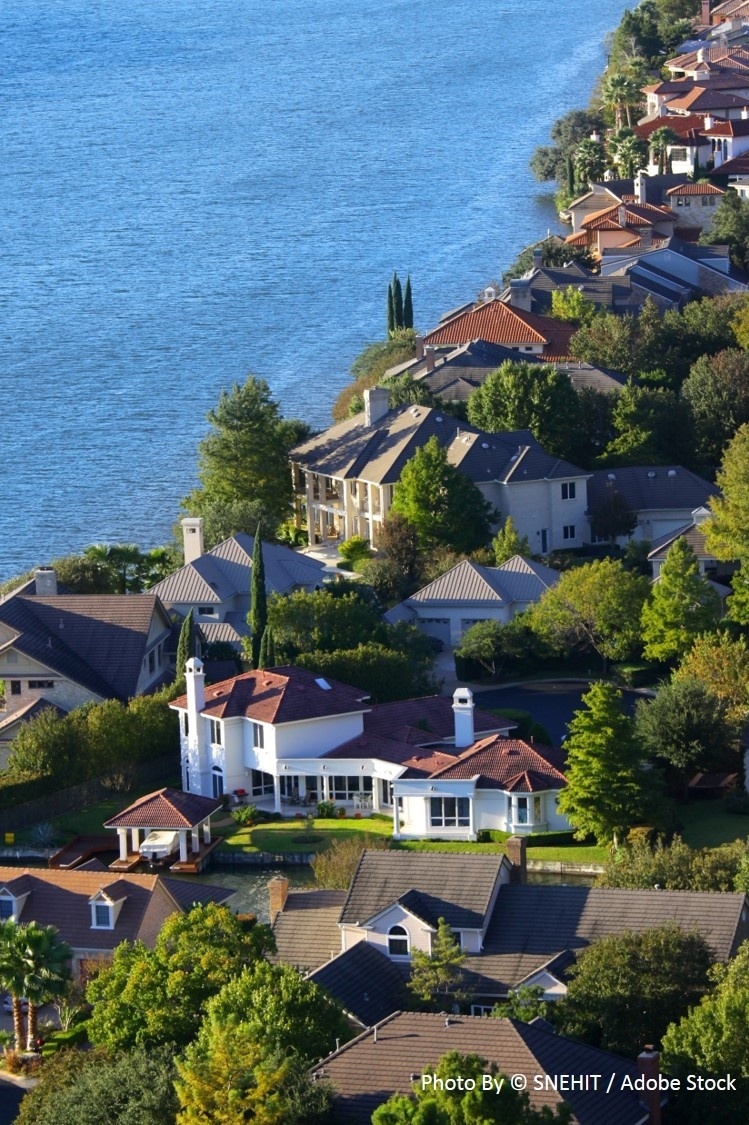 An aerial view captures luxury homes with tile and shingle roofs nestled along a scenic blue lake shoreline.