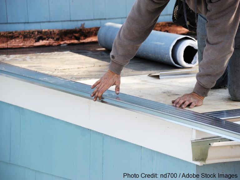 A worker installs metal flashing along a roof eave as part of a professional roof flashing repair project.