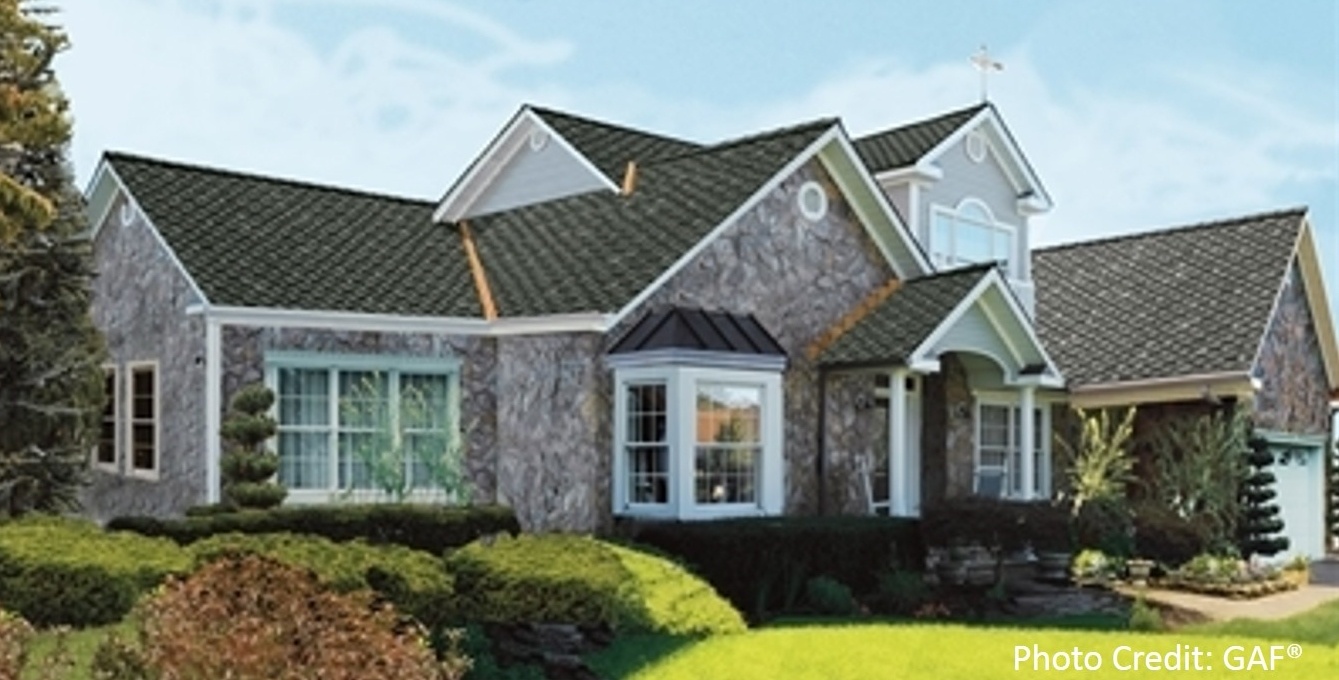 A stone-sided home with a dark green dimensional shingle roof features a bay window and multiple gables.