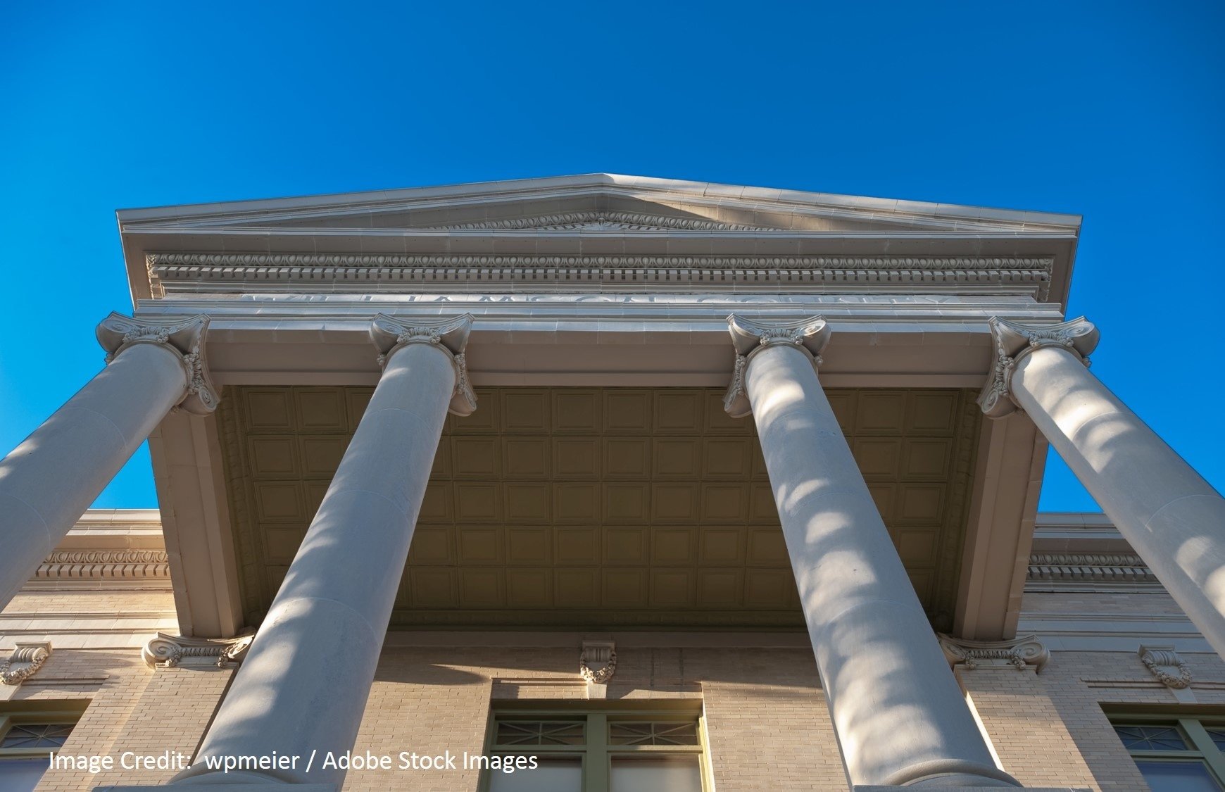 A low-angle view of tall classical columns supporting a triangular pediment against a bright blue sky.
