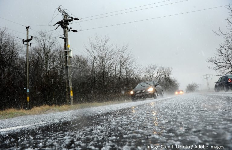 Cars drive along a rural road covered in hail and ice during a winter storm near power lines.