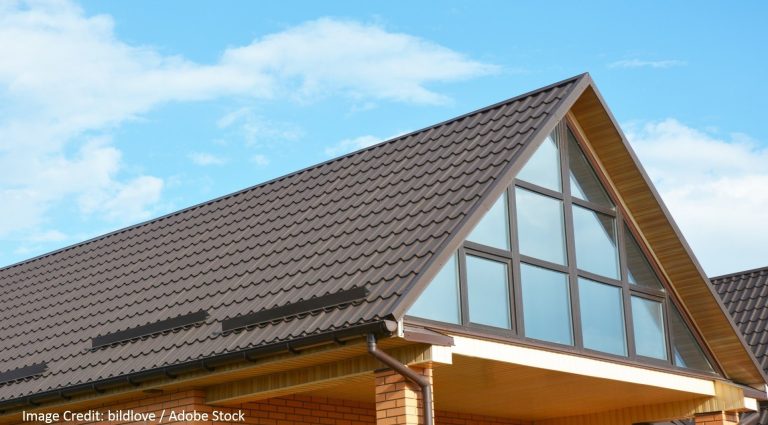 A modern home features a dark tile roof and a triangular gable window with grid-pane glass beneath a blue sky.