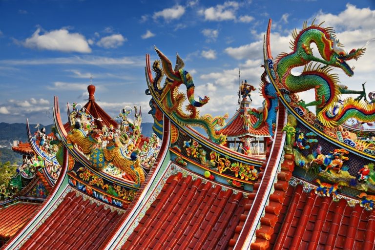 Colorful dragon sculptures decorate the ornate red tile roofline of a traditional Asian temple.
