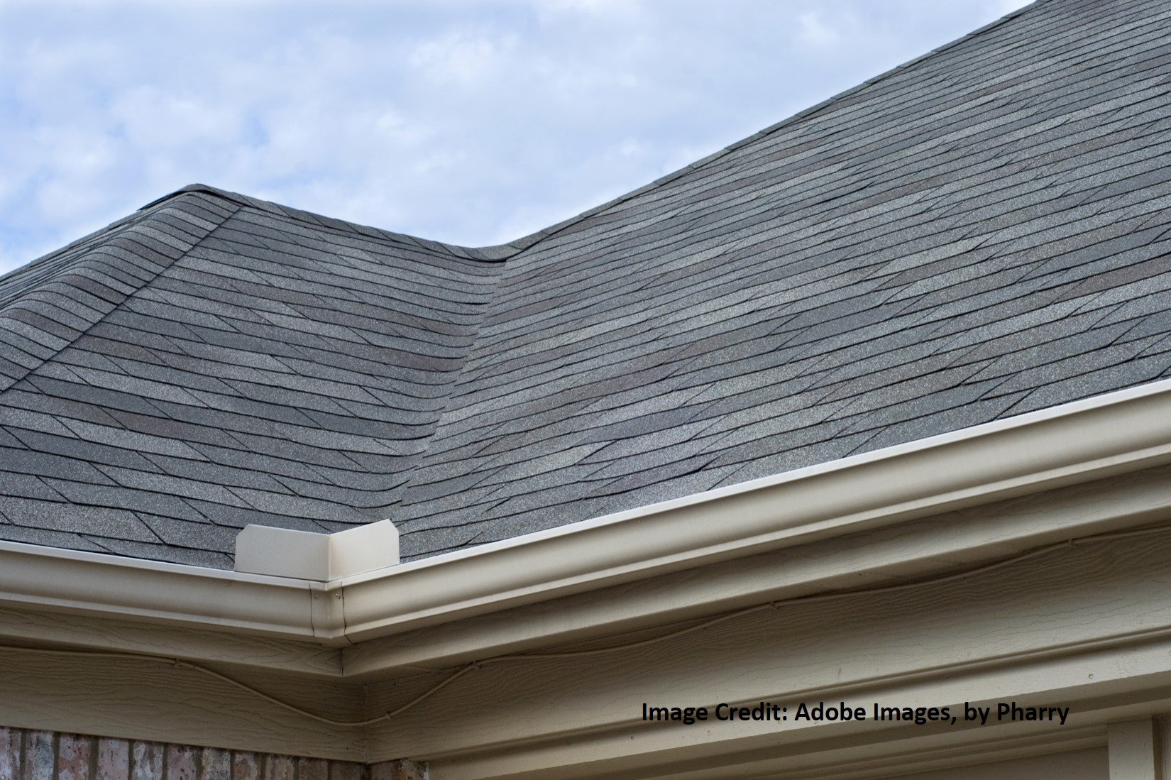 Close-up of gray asphalt shingles covering a residential roof with a defined valley and white rain gutters.