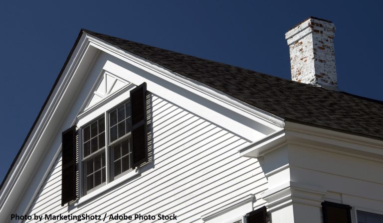 A white clapboard home with black shutters and a dark shingle roof stands beneath a deep blue sky.