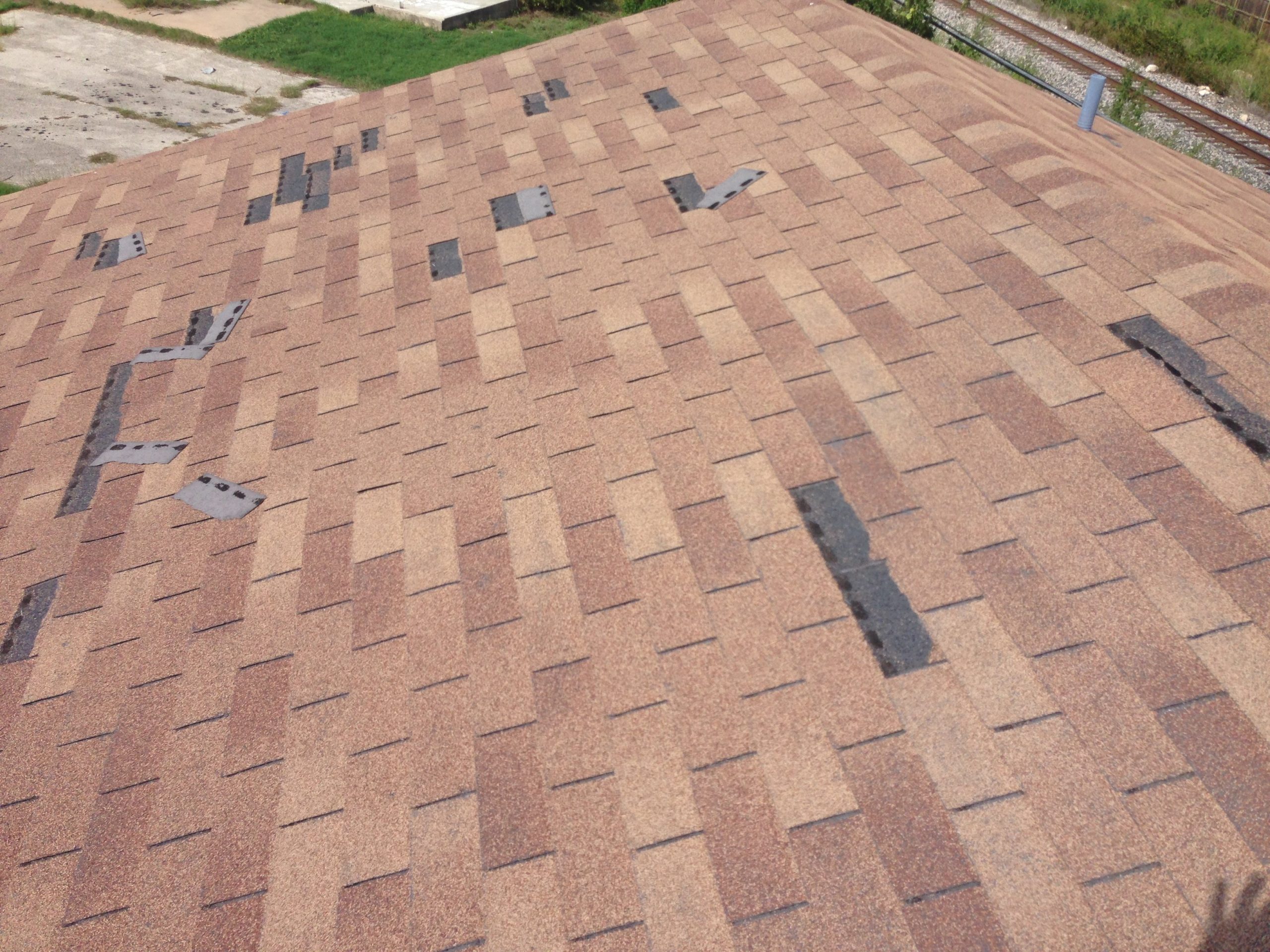 Aging tan shingle roof with numerous curled, lifted, and missing shingles exposing the underlayment beneath.