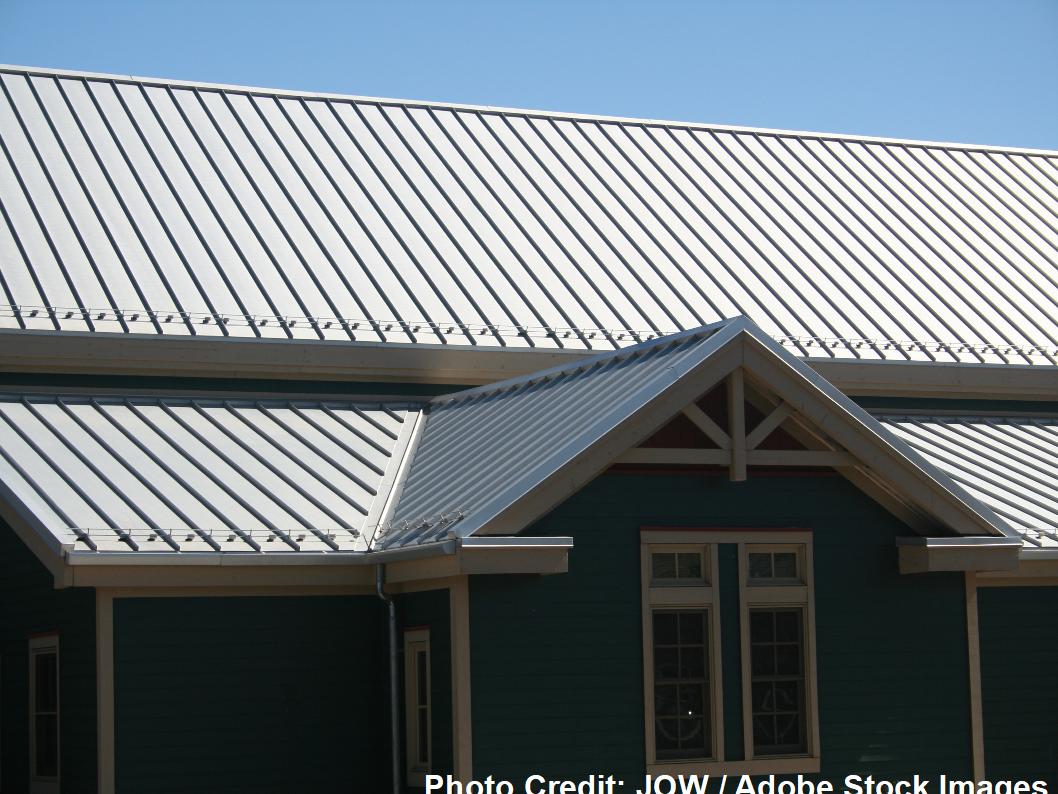 A dark green home features a standing seam metal roof with a gabled peak and exposed wooden support brackets.