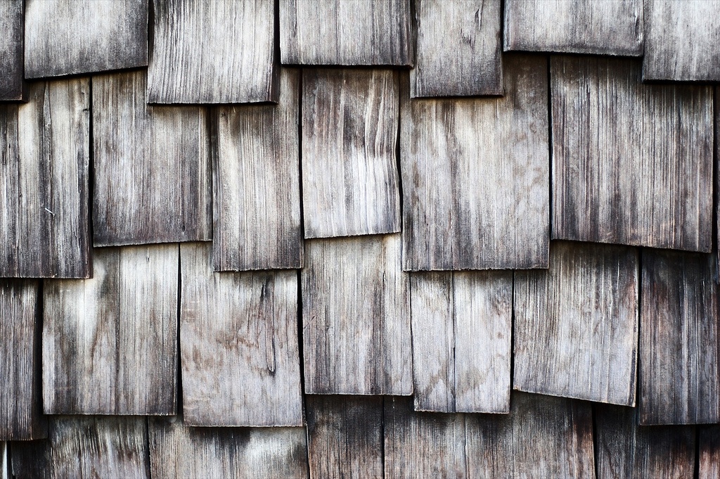Overlapping weathered wood shingles in silvery-gray tones, showing natural grain and a rustic staggered layout.