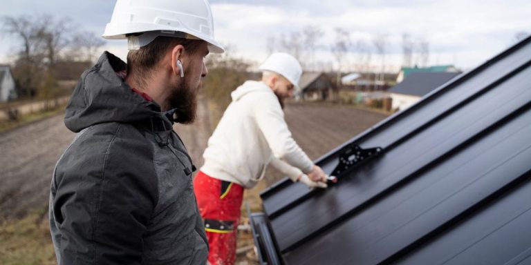 Two workers in hard hats install standing seam metal roof panels as part of a full roof replacement by Longhorn Roofing.