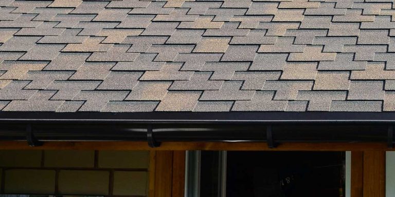 Close-up of layered asphalt roof shingles above a gutter system, illustrating structural complexity when managing double-layer roofing repairs.